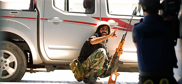 Un rebelde insta a un cámara a ponerse a cubierto en las inmediaciones del hotel Corinthia. | AFP