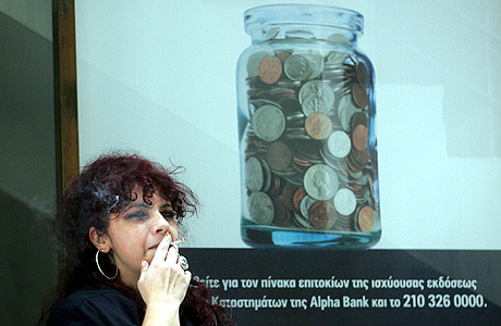 Una mujer griega, junto a un cartel publicitario de un banco. | Efe