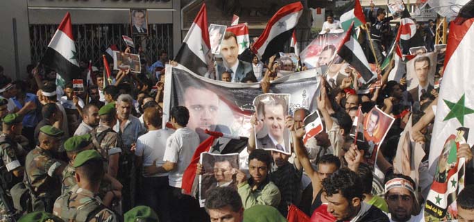 Manifestantes sirios muestran fotos del presidente Bashar Asad durante una protesta. | Efe